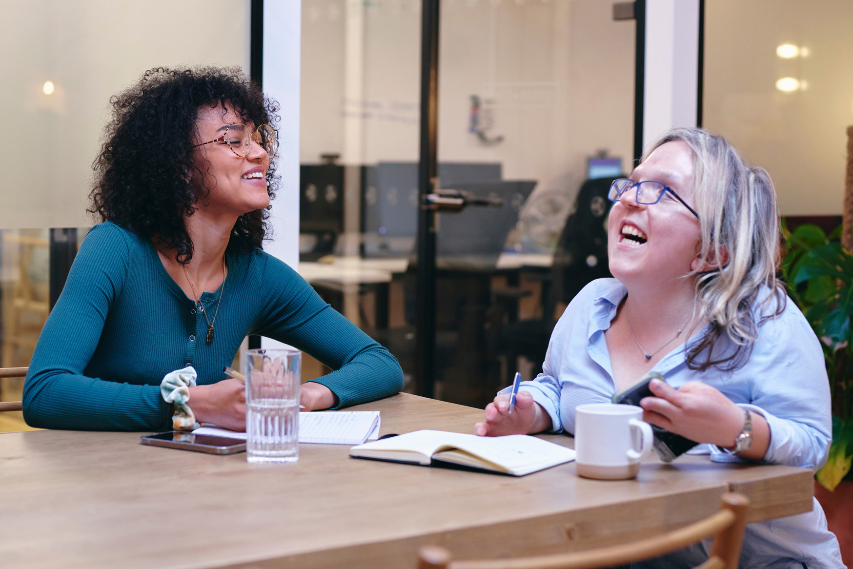 two women sit at a table, laughing together